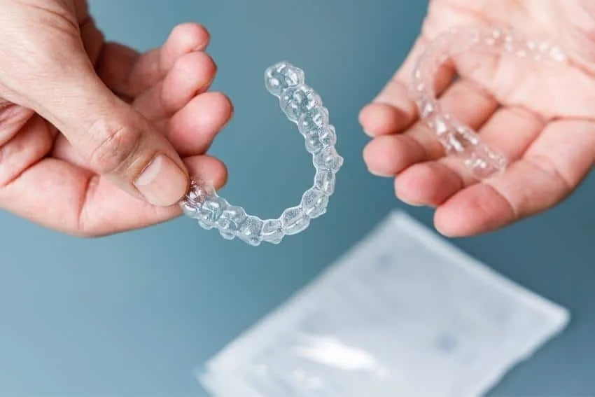 A smiling patient holding a clear Invisalign aligner