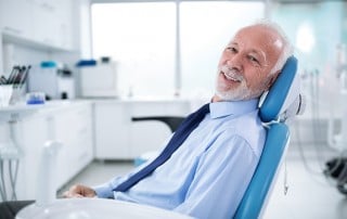 Older man sits in a dental care, awaiting his exam. Even with dentures you should schedule a routine exam to take care of your oral health.