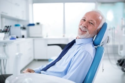Older man sits in a dental care, awaiting his exam. Even with dentures you should schedule a routine exam to take care of your oral health.