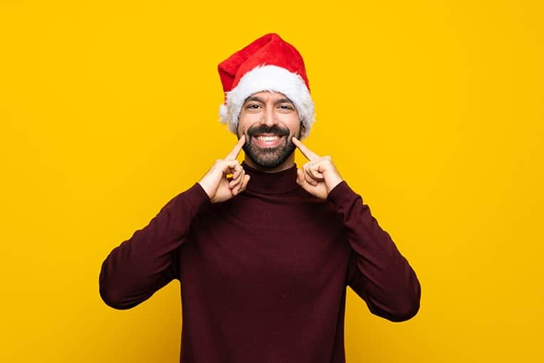 A jolly man with a Santa hat on smiles, showing his grin. How are you taking care of your oral health this holiday season?