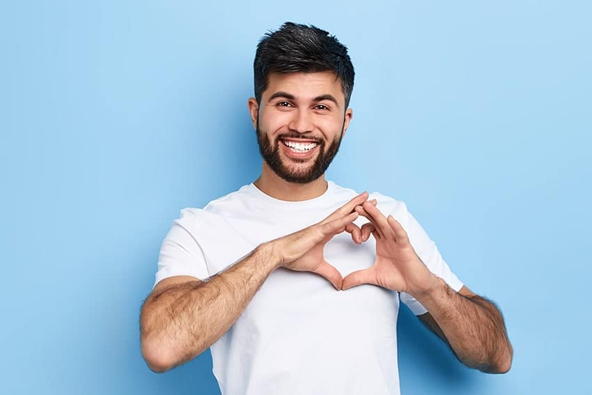 Young bearded man places his hands on his chest in the shape of a heart