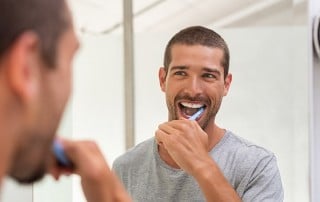 Attractive man stands in front of the mirror while brushing his teeth