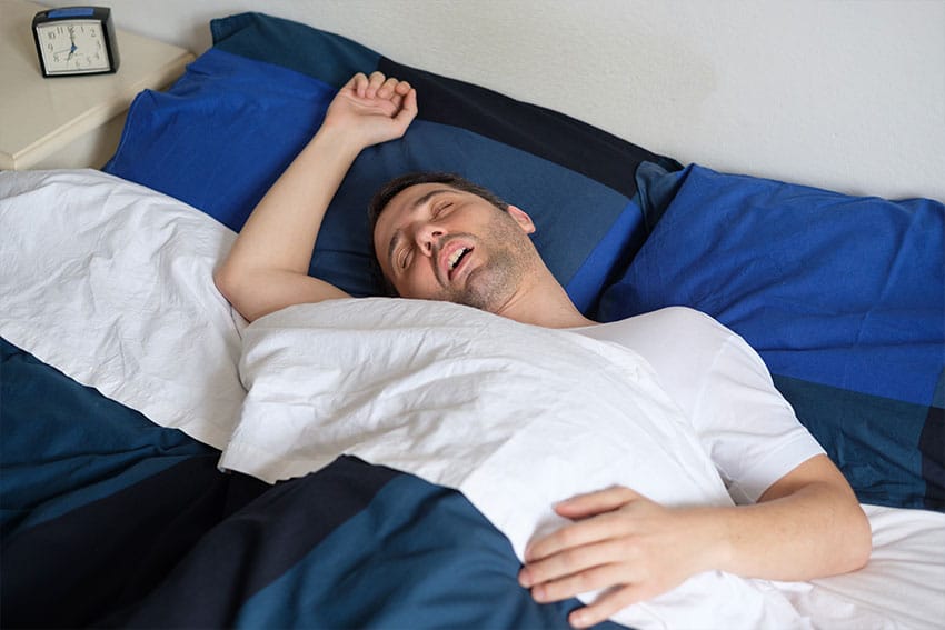 large man sleeping hard in bed, snoring, with his arm over his head