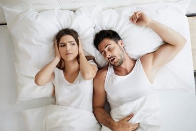 annoyed young woman covers her ears in bed which husband lays next to her snoring 