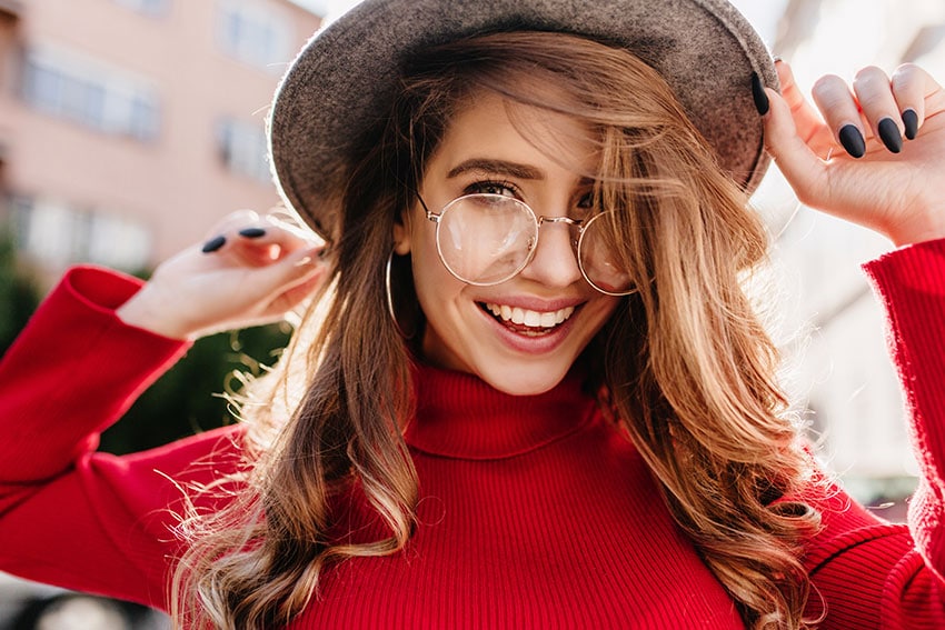 woman in large eye glasses and fancy hat shows off her smile