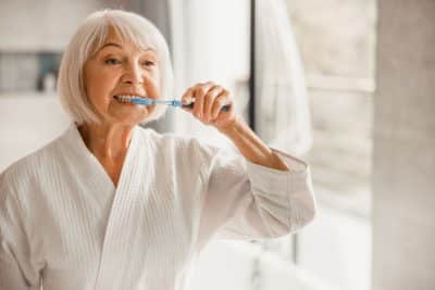 senior woman gently brushing her teeth after having dental implants placed