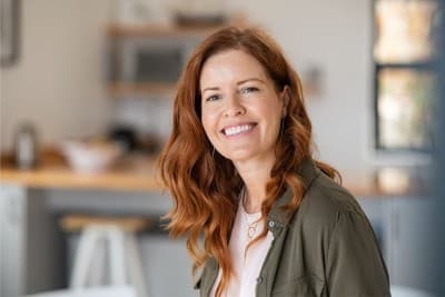A woman with red hair wearing a green button-up sitting and smiling